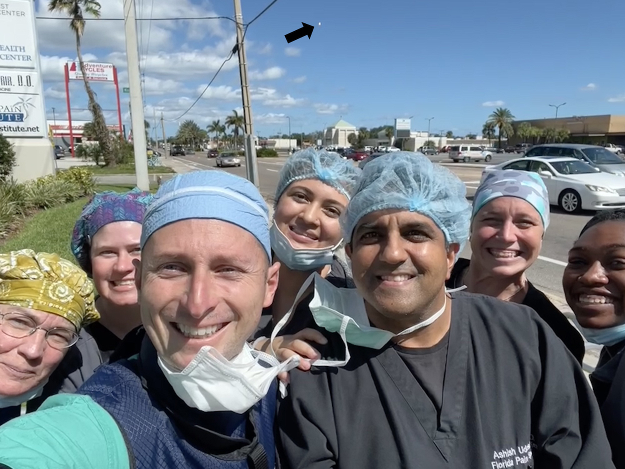 The FPI staff take a group selfie outside the facility. In sky, an arrow points to a distant dot that is a rocket taking off.