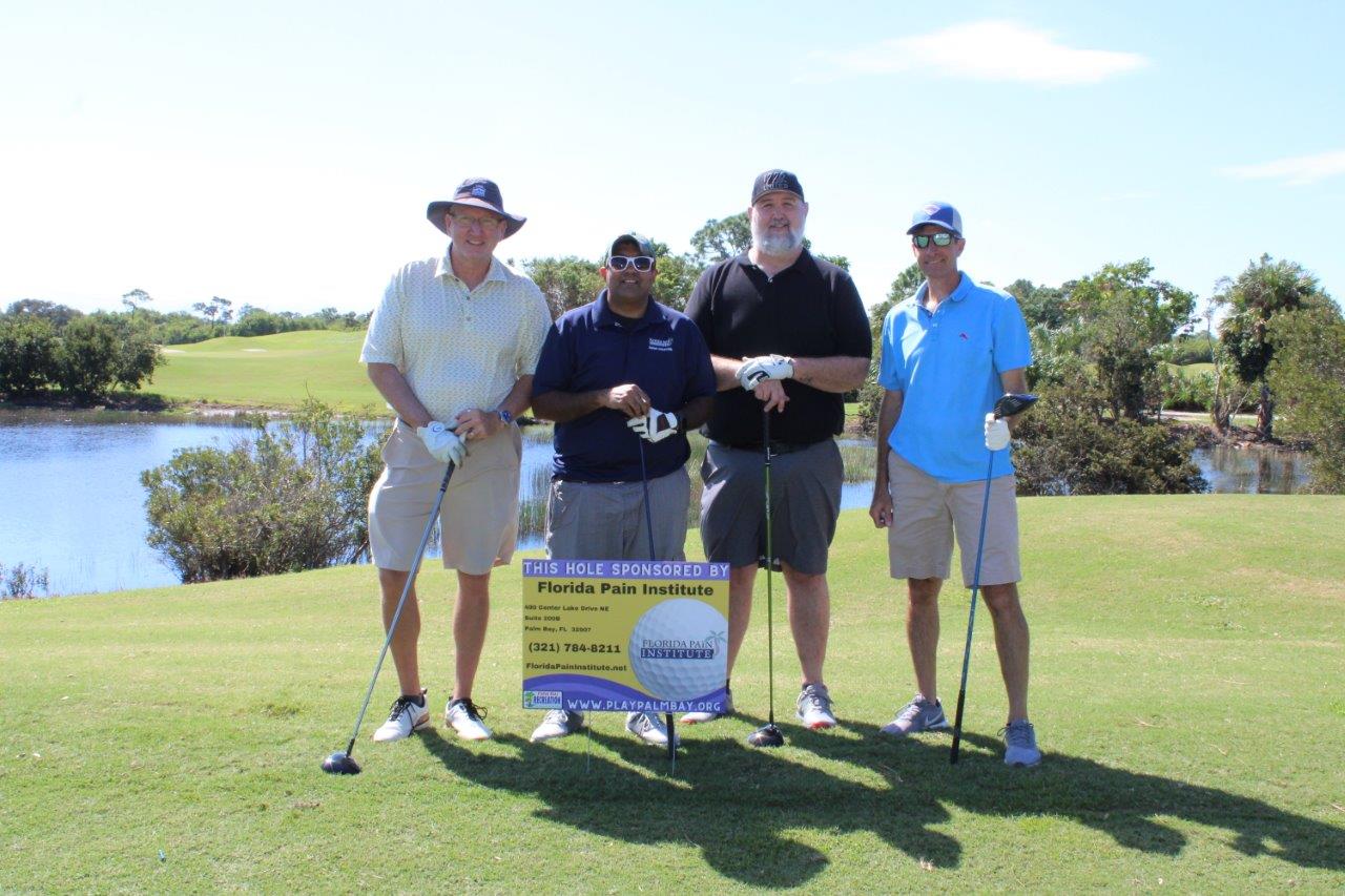 Four men in golf outfits pose together on a green